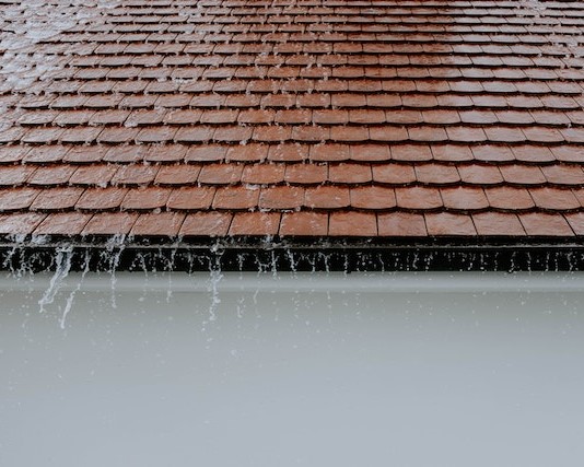 A red tiled roof with water streaming out of it after a thorough power washing.